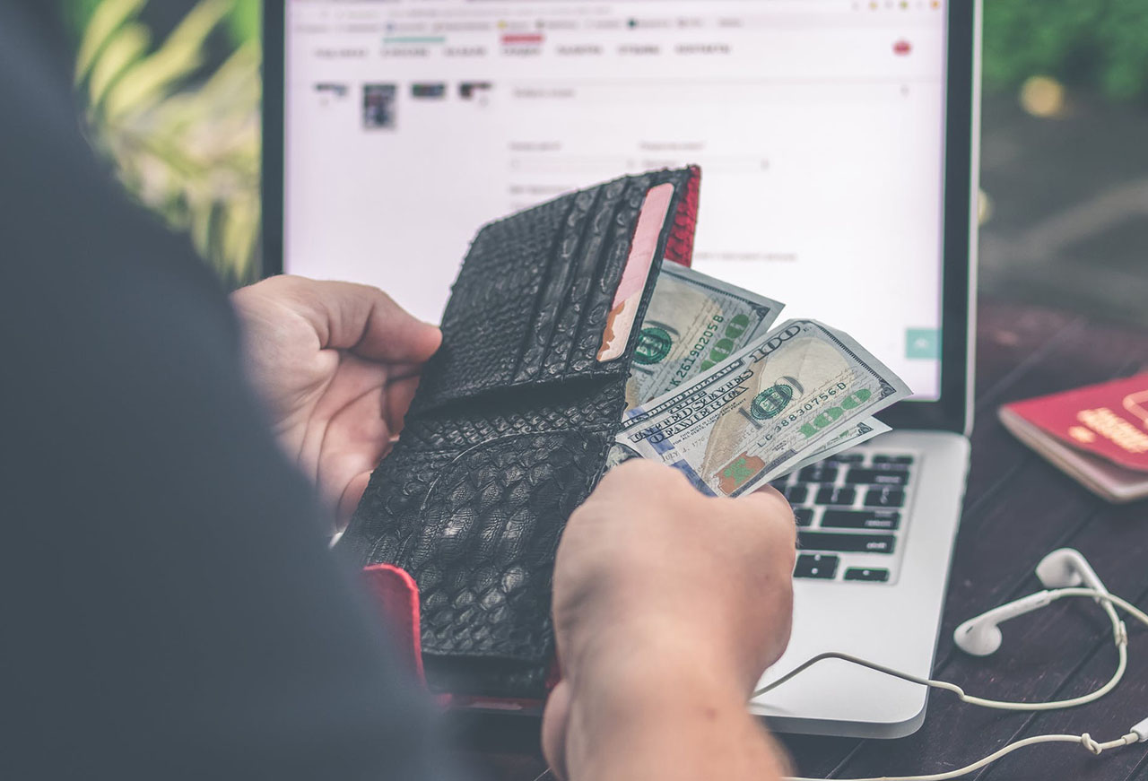 A person pulling money out of their wallet while seated in front of a laptop
